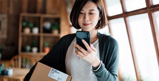 Woman looking at her phone while holding a small package.